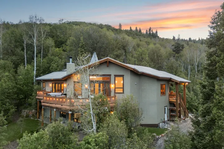 Multi-level property featuring extensive decking, a built-in outdoor spa, exposed wood structural elements, and a stone-clad chimney