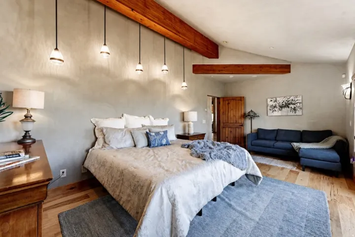 Vaulted ceiling with exposed wood beams, wood-finish flooring, textured wall finish, and a solid wood door