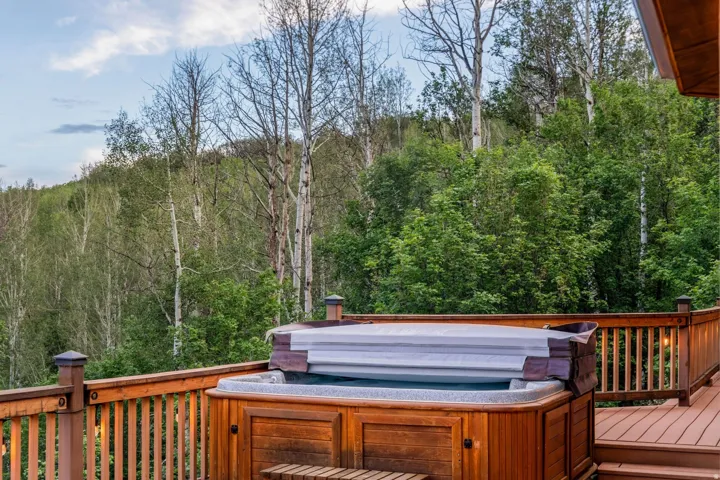 Outdoor hot tub with wood paneling, set on a wood-finish deck with railings and integrated lighting