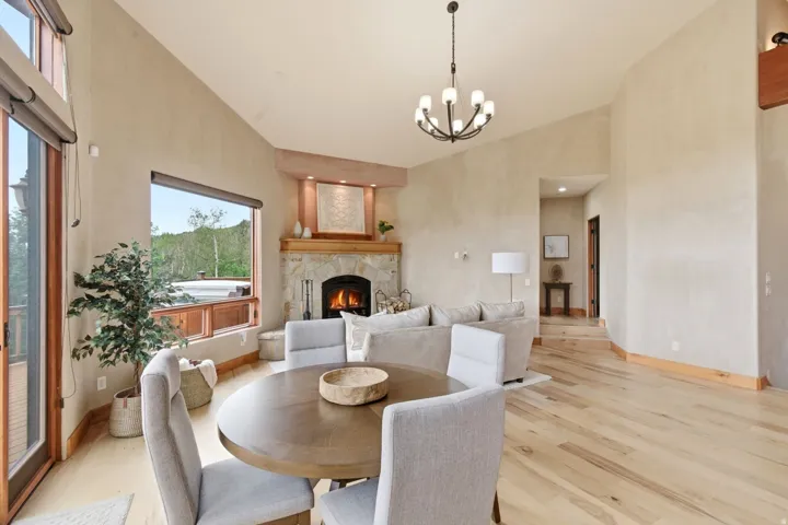 Vaulted ceiling, stone fireplace with a wood mantle, wood-finish flooring, large picture window, and glass sliding door