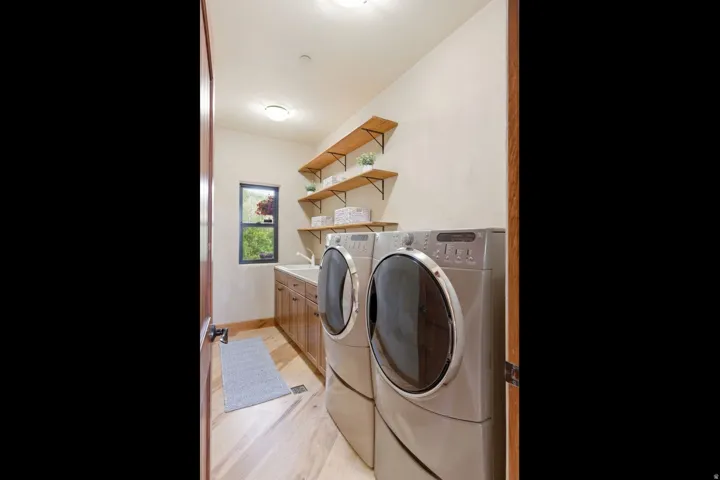 Laundry area featuring wood-finish flooring, built-in cabinetry, a utility sink, and open shelving