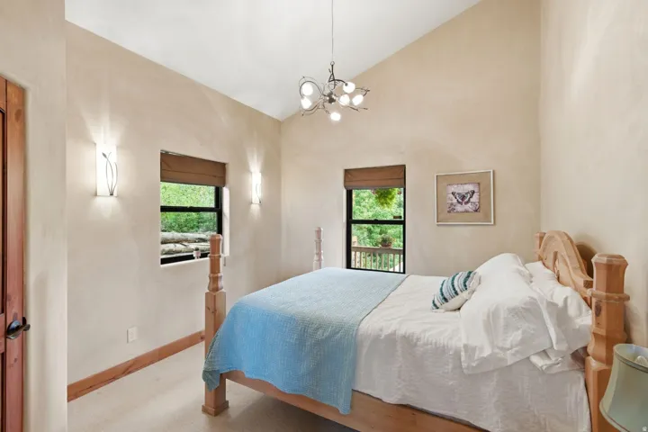 Vaulted ceiling, two windows with window treatments, two wall sconces, ceiling-mounted light fixture, and wood-paneled door