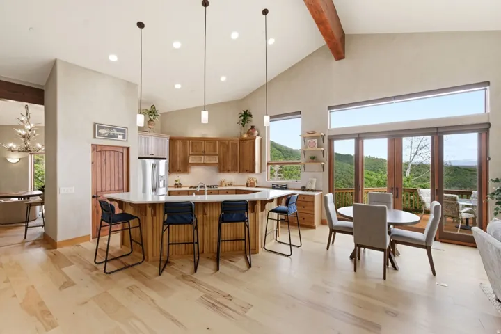 Vaulted ceiling with exposed beam, light wood-finish flooring, full kitchen with stainless steel appliances, white countertop, and expansive glass doors opening to a balcony