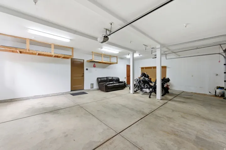 Spacious garage featuring concrete flooring, overhead storage shelving, multiple fluorescent lighting fixtures, and a garage door opener system