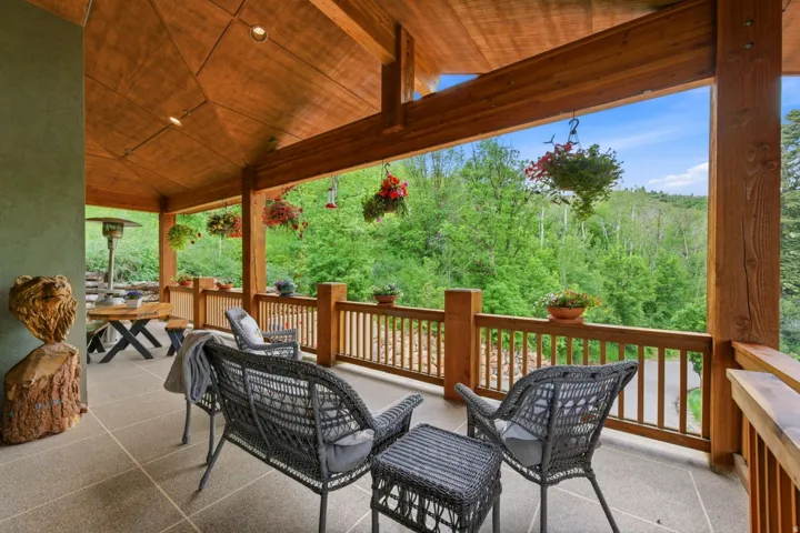 Expansive covered patio featuring a wood-panel ceiling, recessed lighting, wood structural beams, and a wood railing
