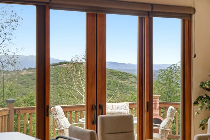 Wood-frame sliding glass doors provide access to an outdoor deck with wood railings, overlooking expansive mountain and tree-covered hill scenery