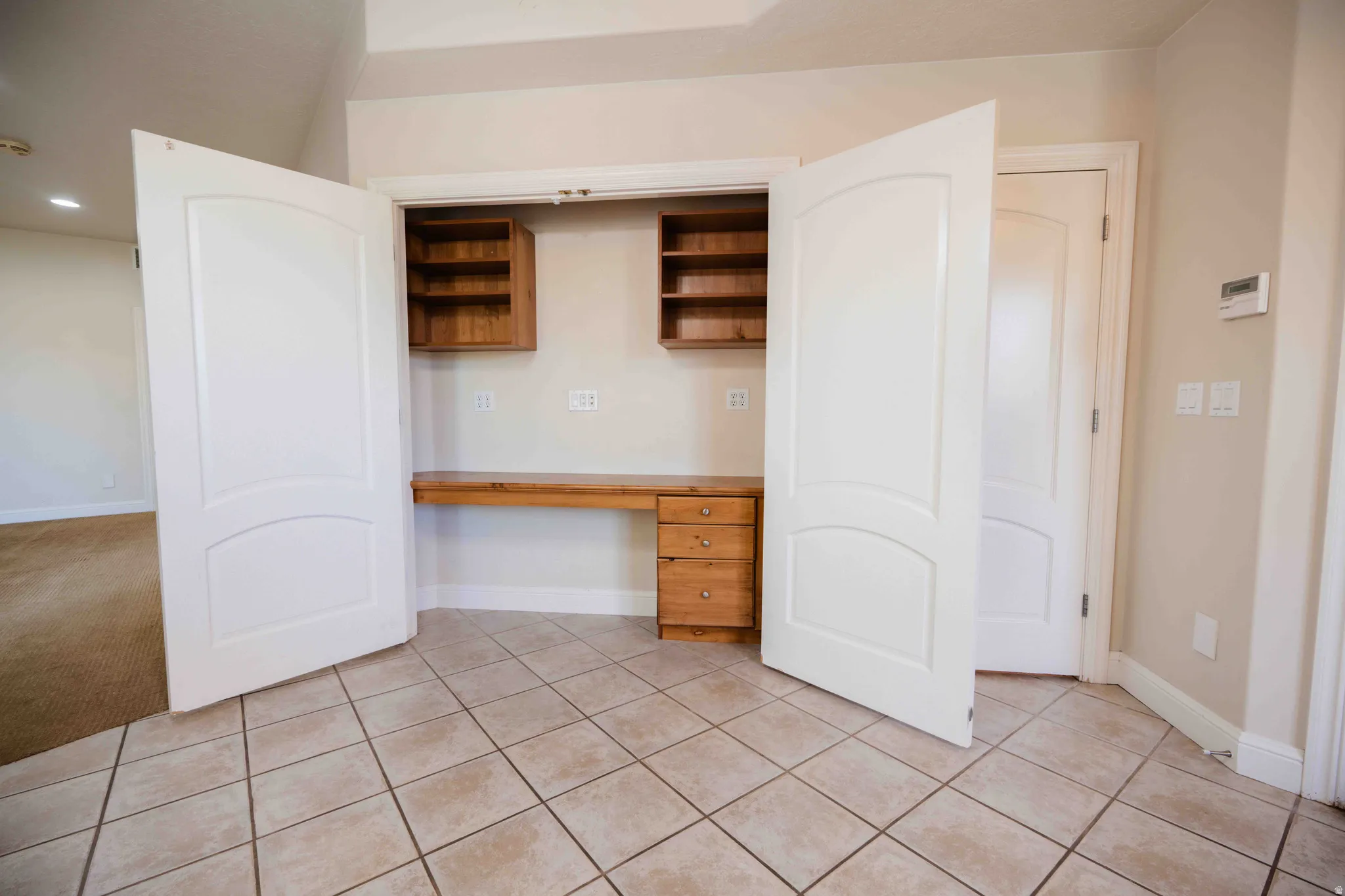 Built-in desk with wood cabinetry, overhead shelving, and tile flooring