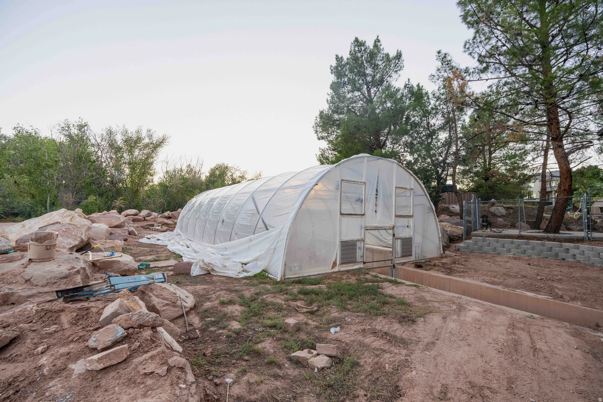 Greenhouse structure with translucent covering, surrounded by natural rock landscaping and mature trees