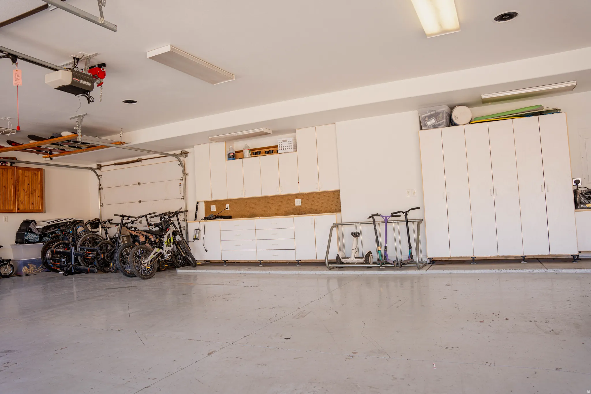 Garage interior with painted concrete floor, white built-in cabinetry, and overhead lighting