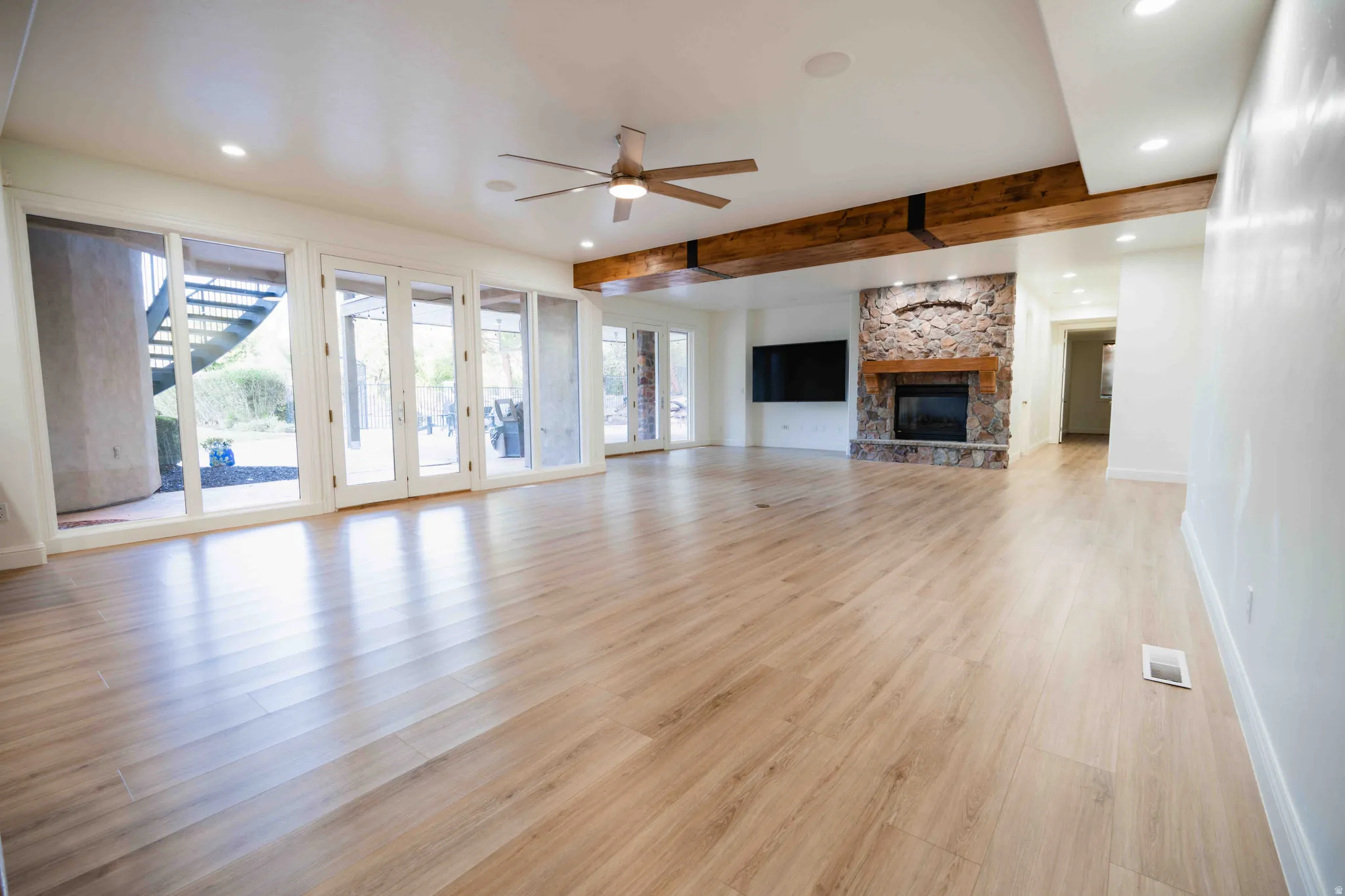 Spacious living area featuring wood-finish flooring, a stone-clad fireplace with a wood mantle, and exposed ceiling beams