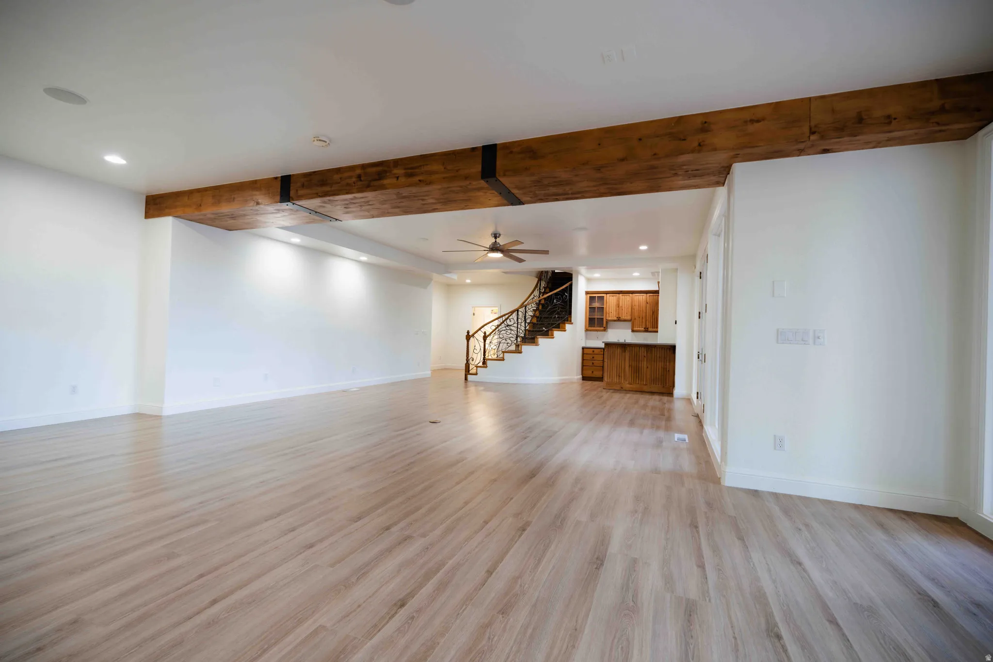 Spacious room featuring wood-finish flooring, exposed ceiling beams, recessed lighting, and a ceiling fan