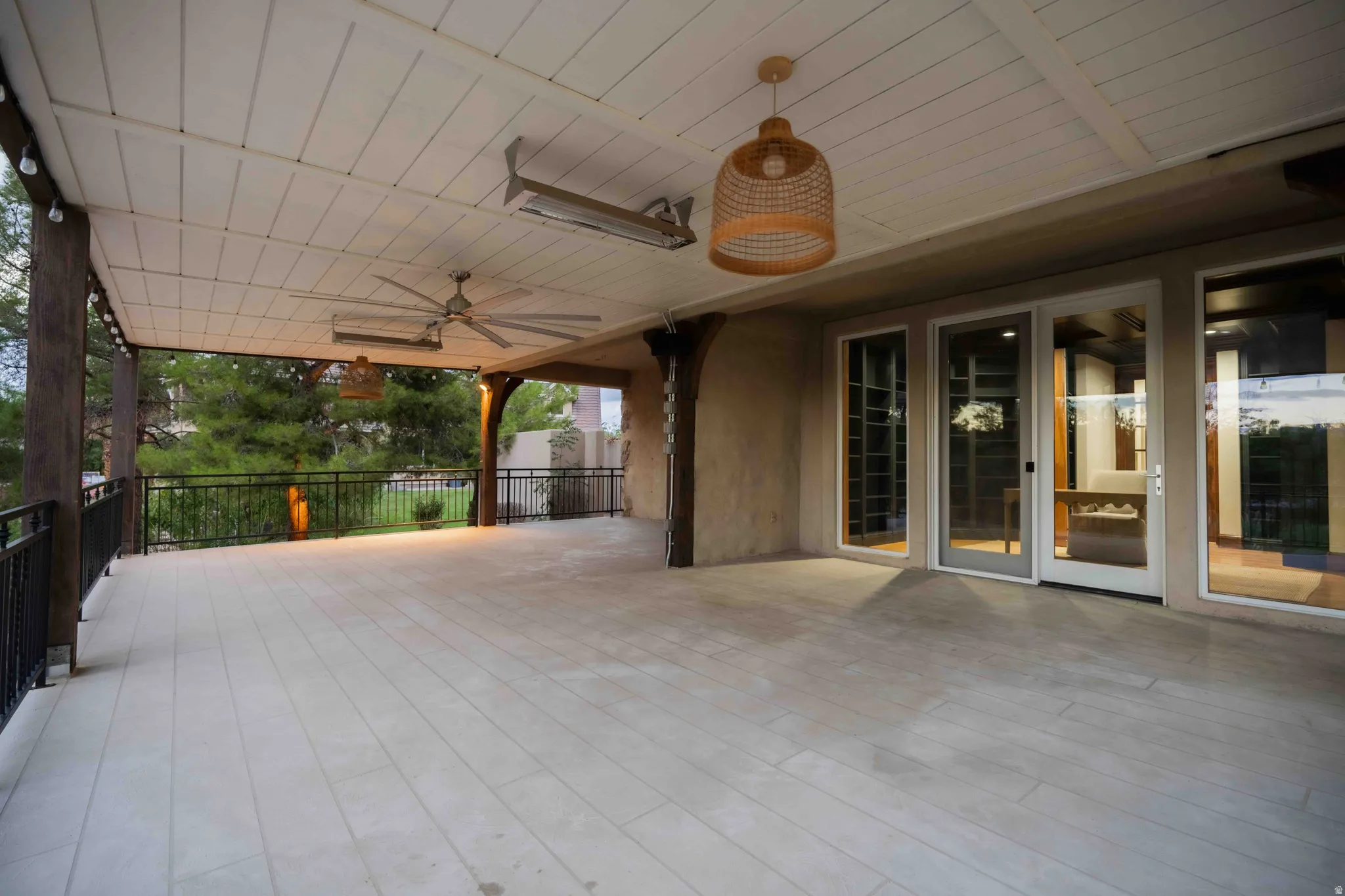 Expansive covered patio featuring a slatted ceiling, tile flooring, two ceiling fans, and multiple glass panel doors