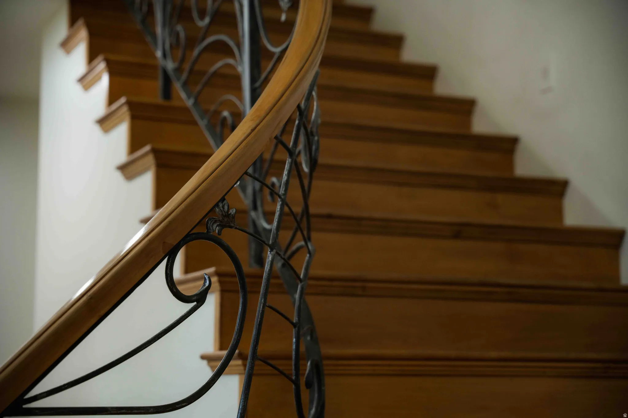 Curved staircase featuring wood treads, wood handrail, and wrought iron balusters