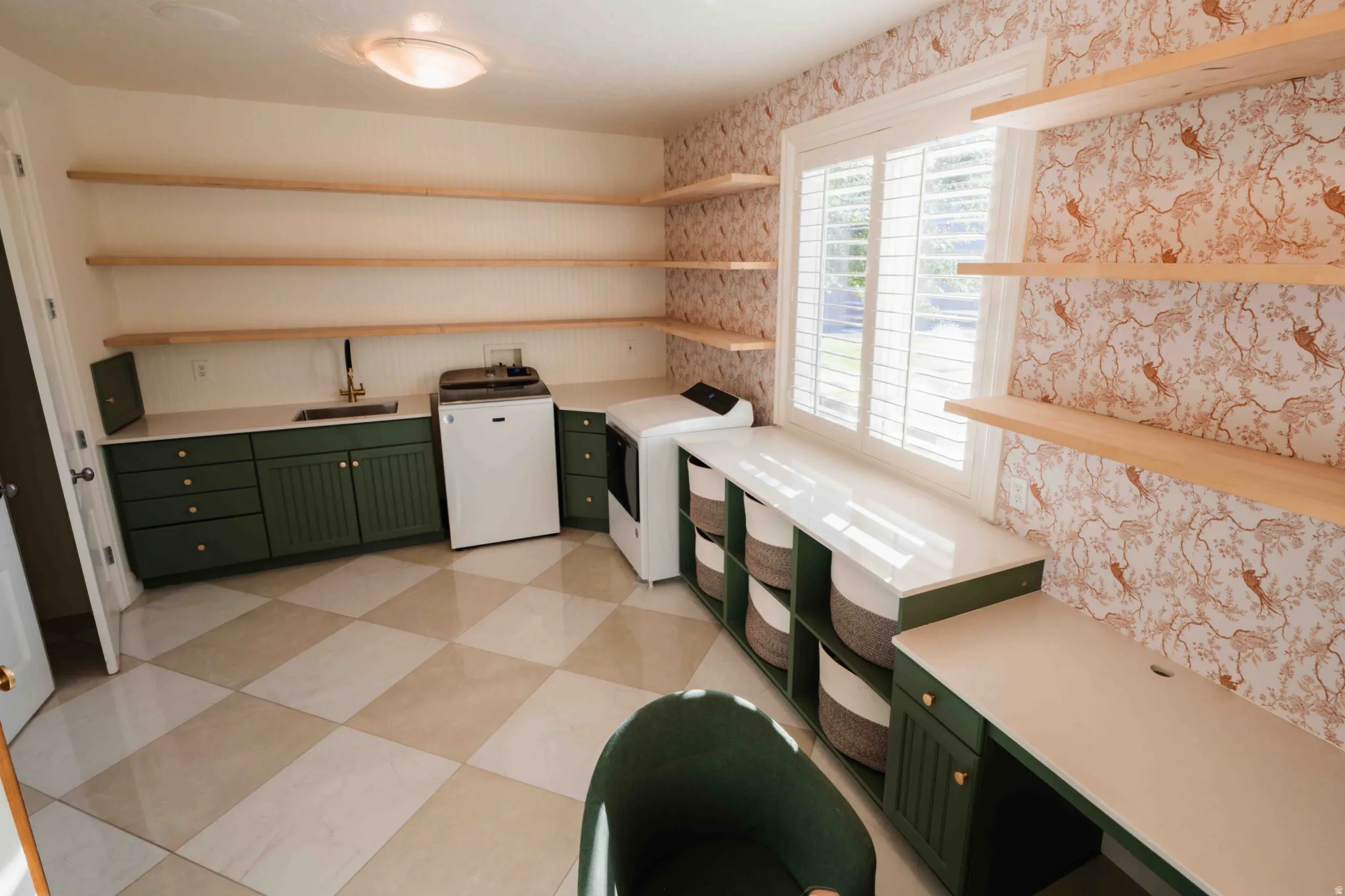 Built-in cabinetry with a sink and gold-tone faucet, open shelving, window with plantation shutters, integrated desk space, and checkered tile flooring