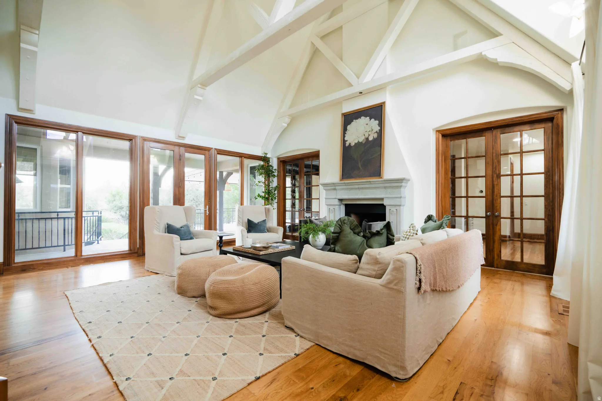 Vaulted ceiling with exposed wood beams, wood-finish flooring, stone fireplace, and French patio doors