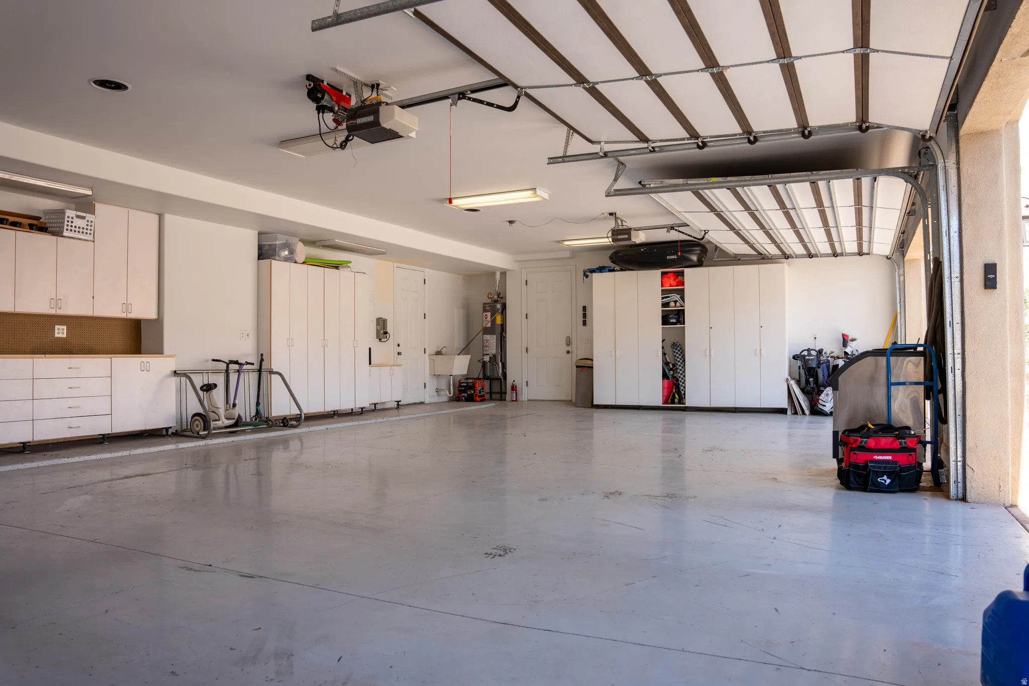 Spacious garage with light gray flooring, white cabinetry, a utility sink, and overhead lighting