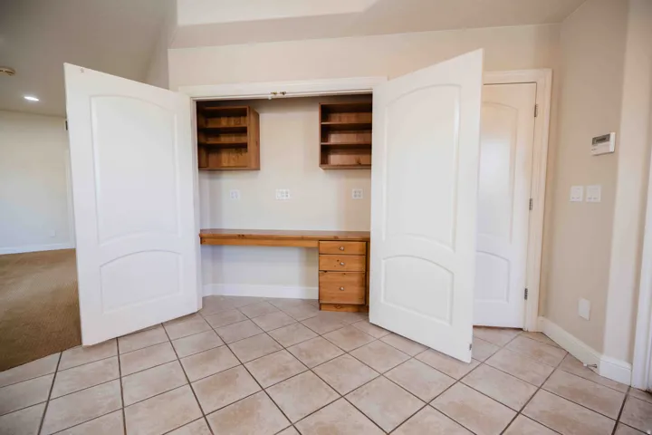 Built-in desk with wood cabinetry, overhead shelving, and tile flooring