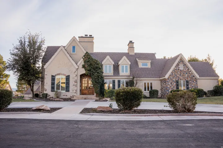 Stucco exterior featuring stone accents, a multi-gabled roof, decorative window shutters, and a wood entry door