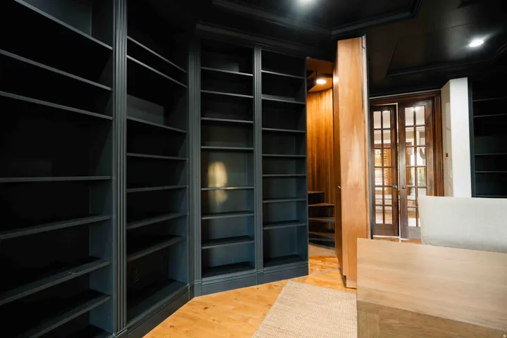 Built-in shelving units in a dark finish, wood-finish flooring, wood French doors with glass panels, and wood-paneled walls. Entrance to the secret room upstairs here