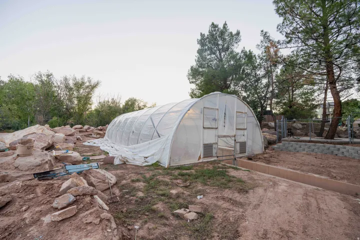 Greenhouse structure with translucent covering, surrounded by natural rock landscaping and mature trees