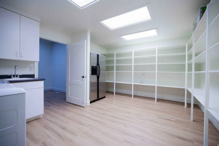 Spacious utility room featuring extensive built-in shelving, wood-finish flooring, recessed lighting, white cabinetry with a sink, and a stainless steel refrigerator