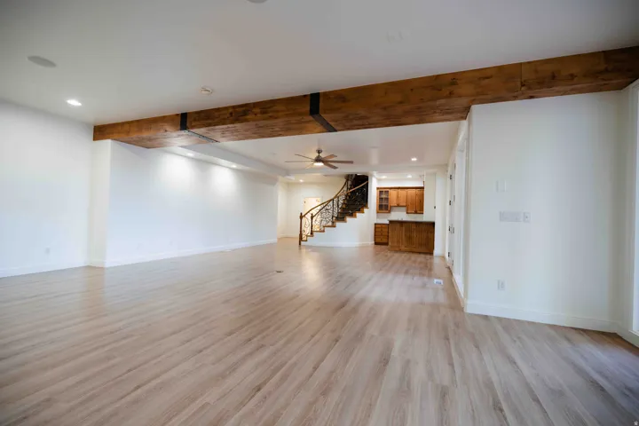 Spacious room featuring wood-finish flooring, exposed ceiling beams, recessed lighting, and a ceiling fan