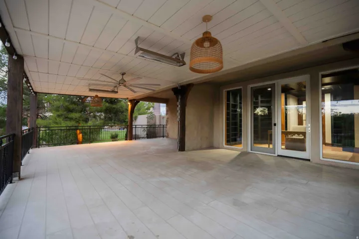 Expansive covered patio featuring a slatted ceiling, tile flooring, two ceiling fans, and multiple glass panel doors
