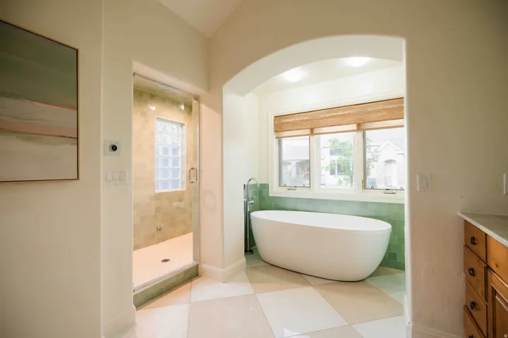 Arched entryway to a bathroom featuring a free-standing soaking tub, three-panel window with woven blinds, and a tiled shower with a glass block window