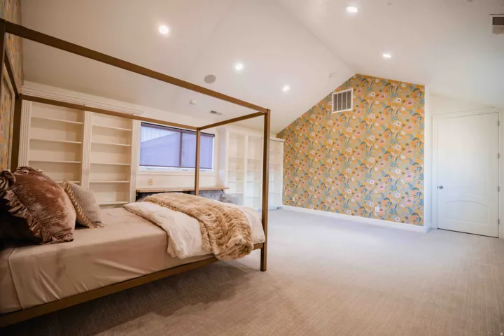 Vaulted ceiling with recessed lighting, built-in shelving, patterned accent wall, and a window with blinds