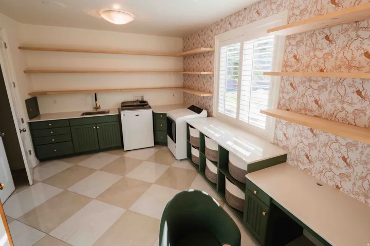 Built-in cabinetry with a sink and gold-tone faucet, open shelving, window with plantation shutters, integrated desk space, and checkered tile flooring