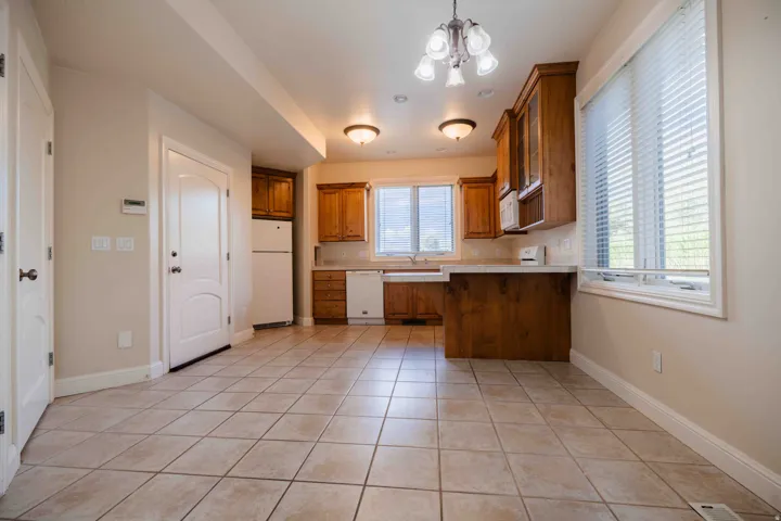basement casita Kitchen with tile flooring, wood cabinetry, built-in dishwasher, and two windows with blinds