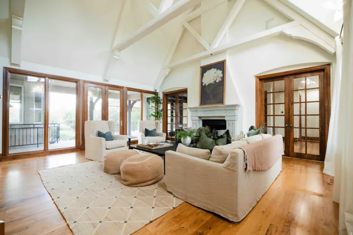 Vaulted ceiling with exposed wood beams, wood-finish flooring, stone fireplace, and French patio doors