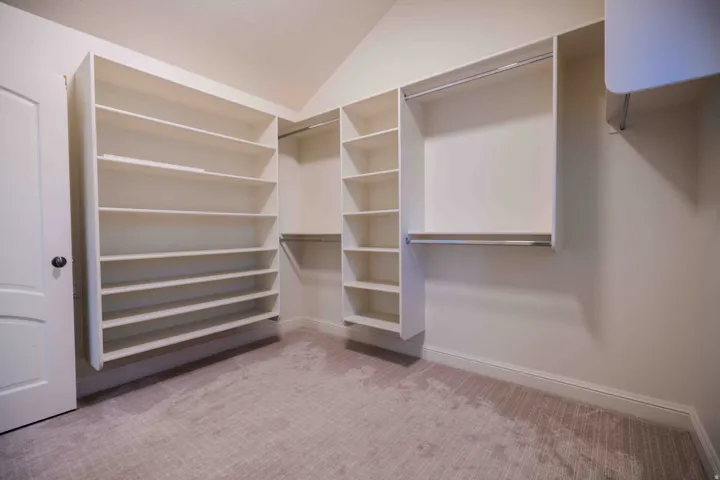 Custom closet system with extensive shelving, multiple hanging rods, vaulted ceiling, and carpeted flooring