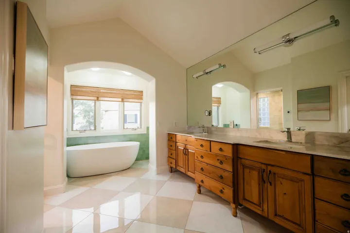 Arched entryway to a freestanding soaking tub, dual vanity with wood cabinetry, light-toned countertop, and checkered floor tiles