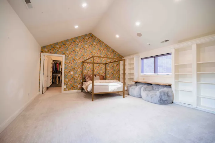 Vaulted ceiling with recessed lighting, built-in shelving, window with roller shades, and a walk-in closet