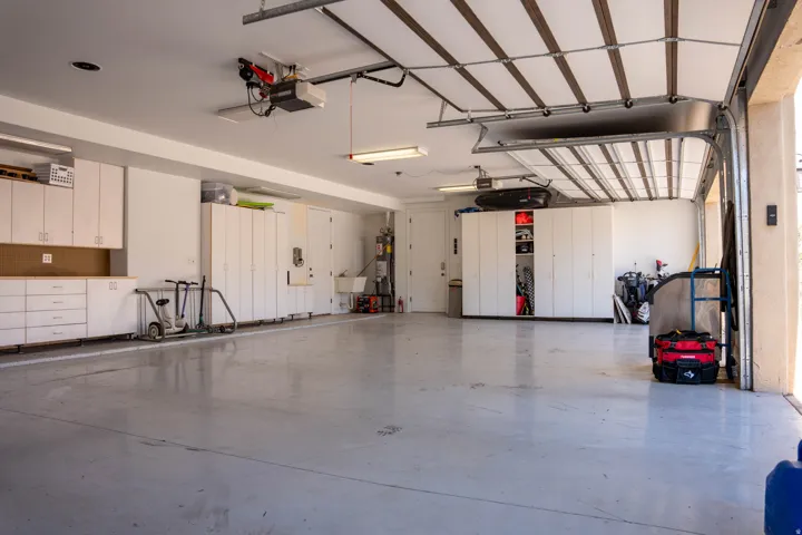 Spacious garage with light gray flooring, white cabinetry, a utility sink, and overhead lighting