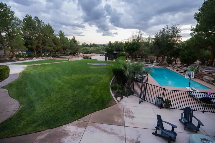 Expansive lawn, large swimming pool, surrounding mature trees, concrete patio, and security fencing
