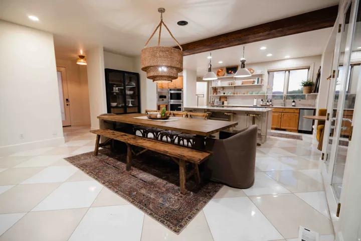 Open-concept kitchen and dining area featuring a tiered woven chandelier, exposed wood beams, and a kitchen island with pendant lighting