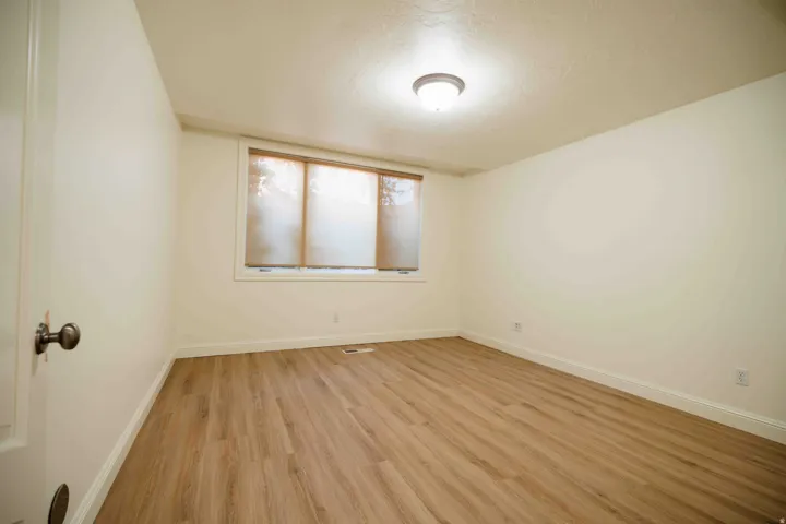 Room featuring wood-finish flooring, a window with roller shades, and a flush-mount ceiling light