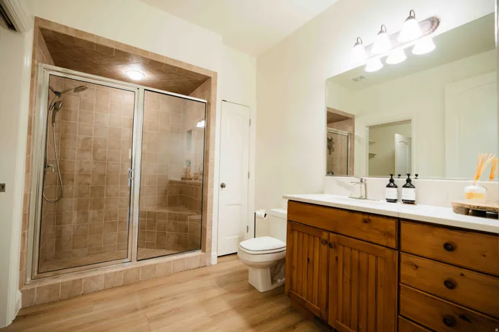 Tiled walk-in shower with a built-in bench, wood-finish flooring, a wood vanity with integrated storage, a white countertop, and a large wall-mounted mirror