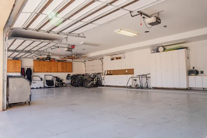 Spacious three-car garage featuring multiple built-in storage cabinets, a workbench with overhead storage, and an automatic garage door opener