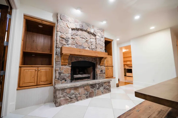 Stone-clad fireplace with a wood mantle, built-in shelving with cabinetry, recessed lighting, and checkered tile flooring