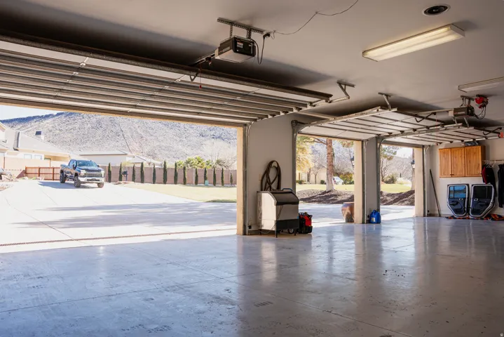 Spacious three-car garage featuring automatic openers, overhead fluorescent lighting, and built-in wood cabinetry