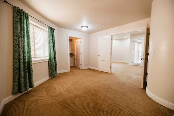 Carpeted room with a curved wall, multiple doorways, and a window featuring blinds