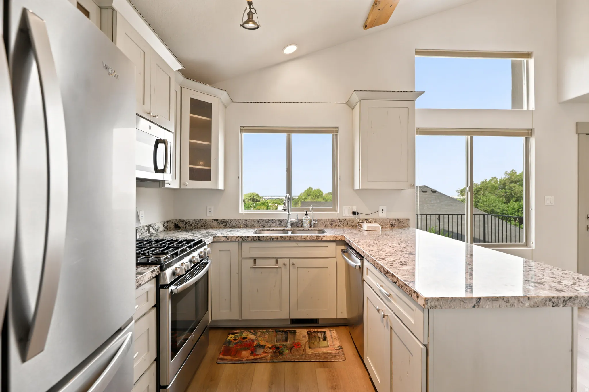 Kitchen featuring vaulted ceilings, stainless steel appliances, light-toned cabinetry, granite countertops, and wood-finish flooring