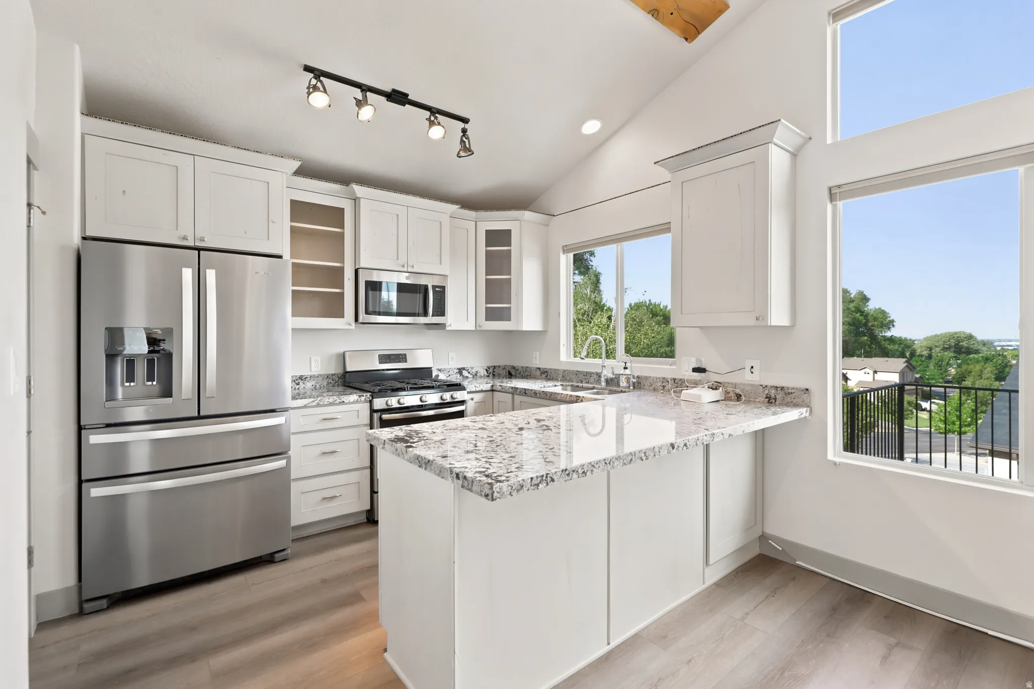 Kitchen featuring vaulted ceilings, wood-finish flooring, white cabinetry, a stainless steel appliance suite, and stone countertops