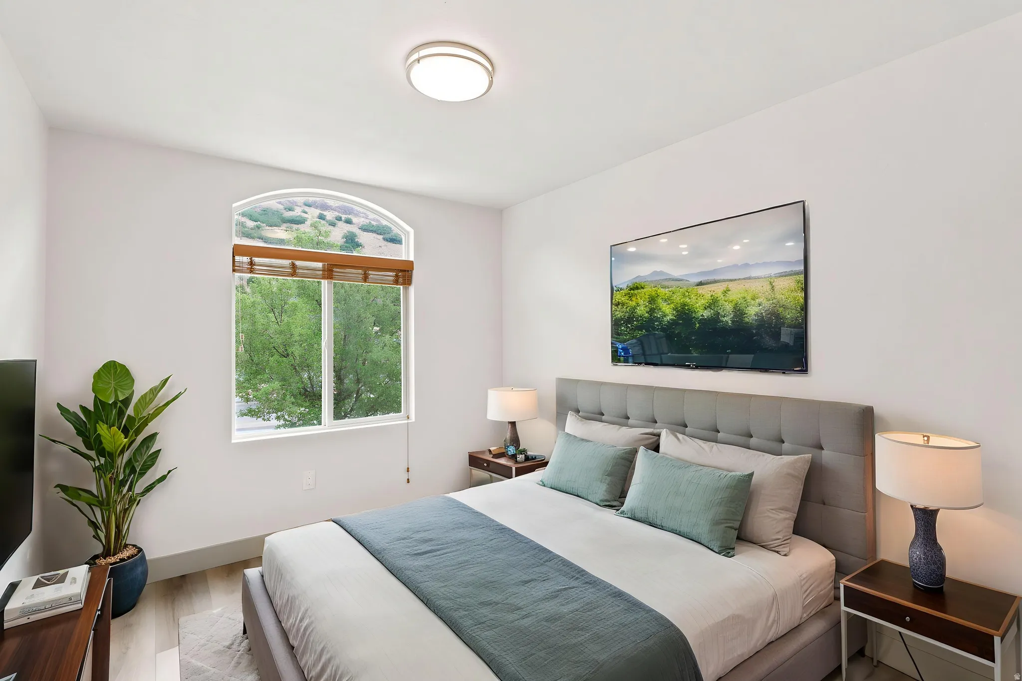 Arched window with wood-finish blinds, light wood-finish flooring, and a flush-mount ceiling light