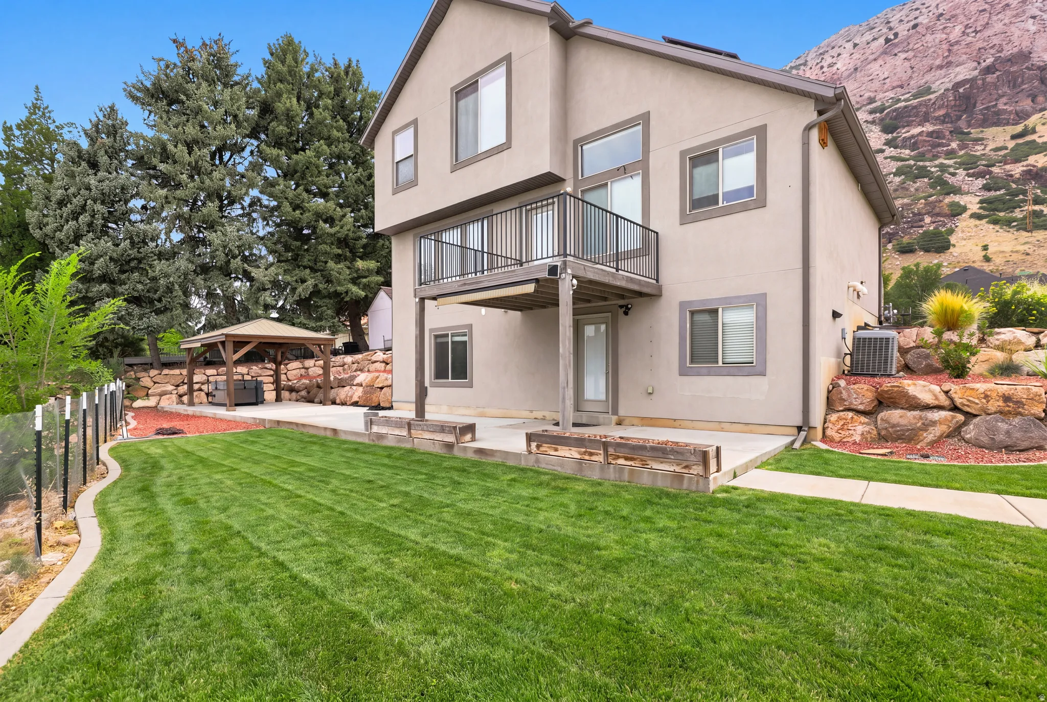 Expansive rear yard featuring a concrete patio, wood-finish raised garden beds, and a covered gazebo structure