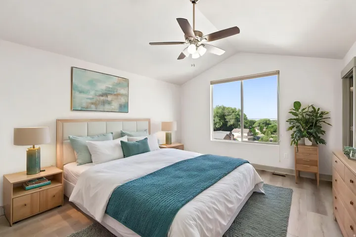 Vaulted ceiling with a ceiling fan, large window, wood-finish flooring, and light-toned walls