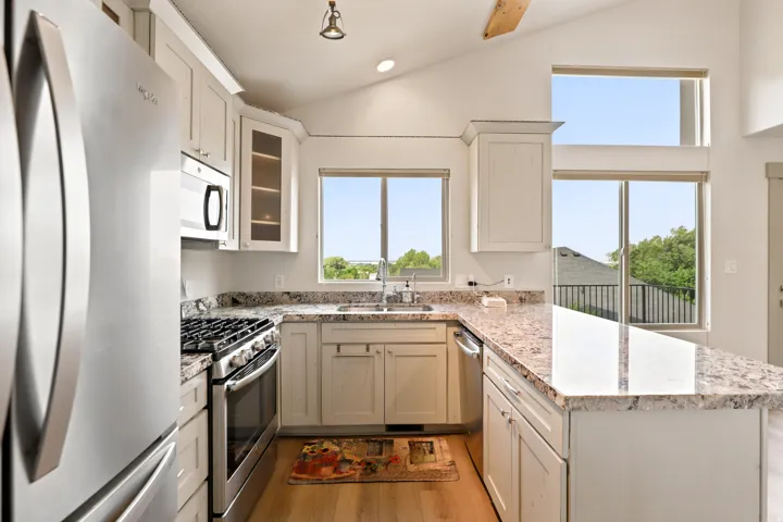 Kitchen featuring vaulted ceilings, stainless steel appliances, light-toned cabinetry, granite countertops, and wood-finish flooring